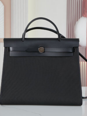 Hermès black canvas bag, carried by one shoulder and one hand.